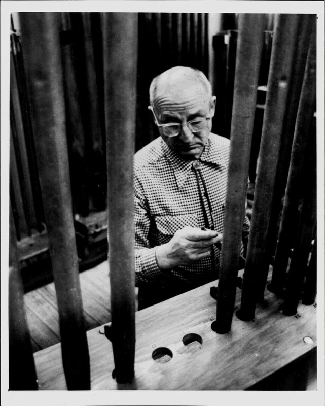 A black and white photograph of an old man working on a pipe organ