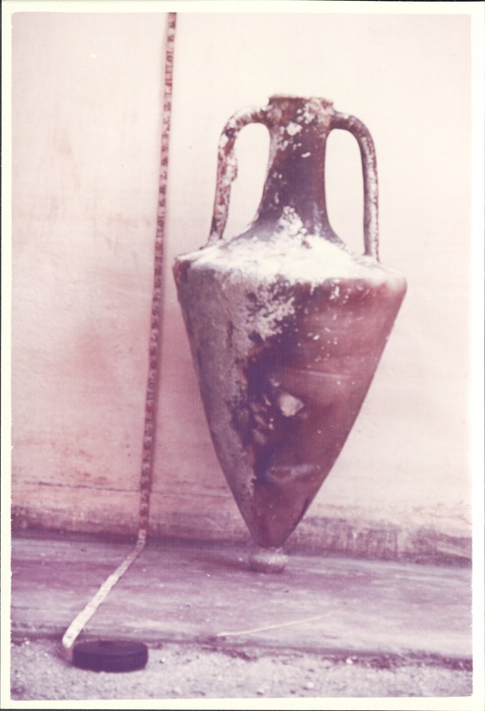 A sepia photograph of a tall Greek or Roman jar (i.e. an amphora) next to a measuring tape