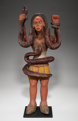 The Mami Wata figurine depicts a woman standing with her hands in the air, with a snake wrapped around her arms as well as another snake wrapped around her torso. This is a display of the spirit's, Mami Wata's, snake-charming abilities.