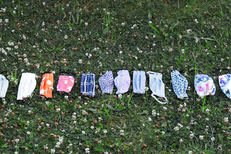 Fabric masks in various colors and prints laid out next to each other outside on the grass