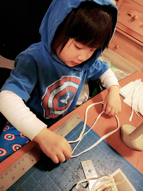 Little Asian girl measuring out the mask ties to be cut for mask-making