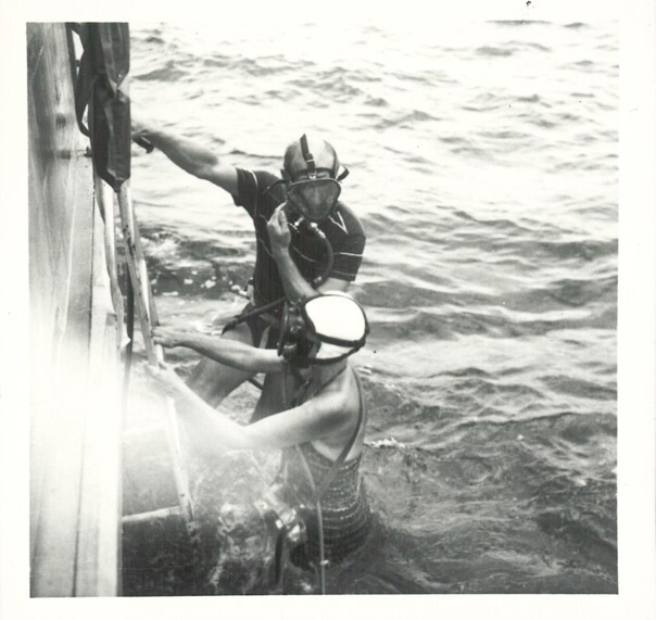 A black and white photograph of a man and a woman about to dive into the sea