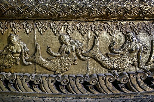 This image shows the carvings of three mermaids on a catafalque, which is the scaffolding of a coffin. These mermaids depicted are that from the Ramayana which are nude females with a tail making up their body from the waist down.