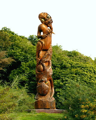 The image shows a large wooden carving that represents the Māori legend of Kupe and Te Wheke. An octopus-like figure can be seen wrapped around towards the bottom of the structure, with another figure towards the top, holding a sort of tool or weapon. 
