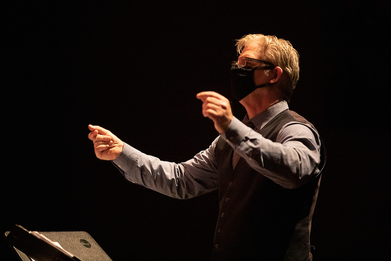 Director Laurence wearing a mask conducting on stage