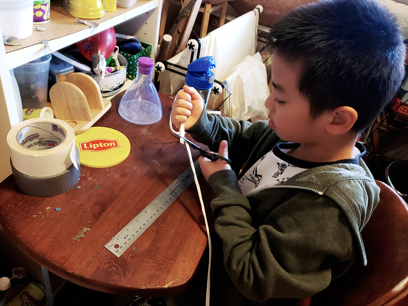 Little Asian boy cutting the elastic for mask-making