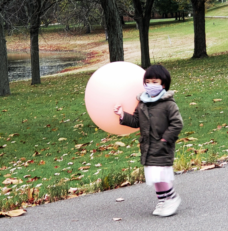 Little Asian girl wearing a mask, holding a super big pink balloon walking around at Otsiningo Park
