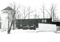 A photography of a factory with a silo surrounded by snow and bare trees