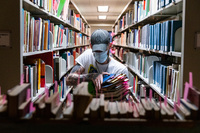 Masked student assistant moving books from the library shelves for relocation