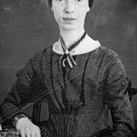 This black and white image of Emily Dickinson shows her wearing a black dress with a thin black scarf. She has her hair tied in the back and is looking at the viewer with a blank face. 