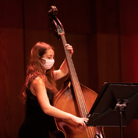 Band member Abigail wearing a mask playing the acoustic bass on stage