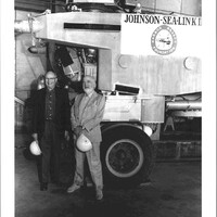 A black and white photograph of two men standing in front of a submersible