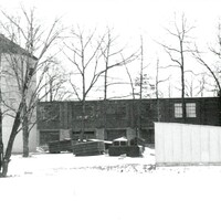 A photography of a factory with a silo surrounded by snow and bare trees