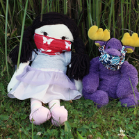 A stuffed doll and a stuffed purple moose wearing fabric masks, sitting out in the grass