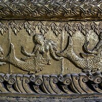 This image shows the carvings of three mermaids on a catafalque, which is the scaffolding of a coffin. These mermaids depicted are that from the Ramayana which are nude females with a tail making up their body from the waist down.