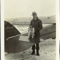 A black and white photograph of a man with a dog standing next to an airplane