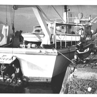 A black and white photograph of a boat docked at a port with a man and a woman