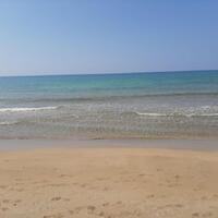 A beige sandy beach with footprints imprinted in the sand. Meeting the sand at the beach is crystal clear, calm, blue water. 