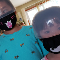 Two young Asian kids wearing a makeshift clear plastic helmet covering over their eyes, along with their fabric black masks