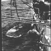 A black and white photograph of several men on a boat lowering a submersible into the water